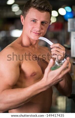 A muscular man with naked torso in a perfume shop smelling toilet water