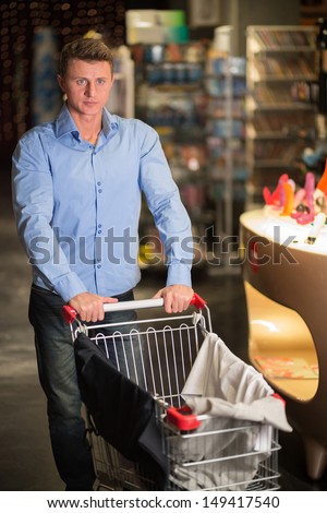 Young man with a clothes in the cart in the store for adults
