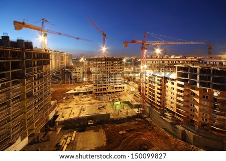 Lots of tower cranes build large residential buildings at night.