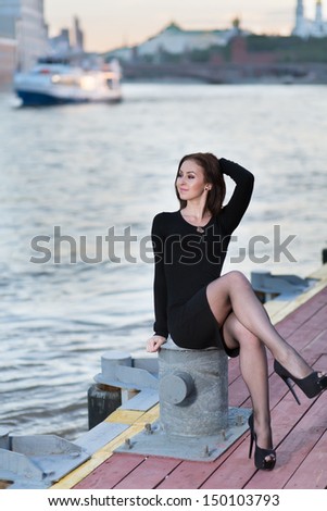 A young woman is sitting cross-legged on the device for the mooring of vessels on the waterfront