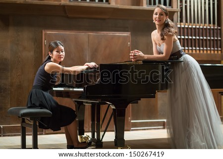 Woman pianist sits at the piano and beautiful singer stands next