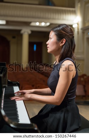 Woman pianist sits at the piano in empty concert hall