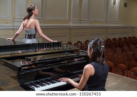 Woman pianist sits at the piano and beautiful singer stands next in empty concert hall