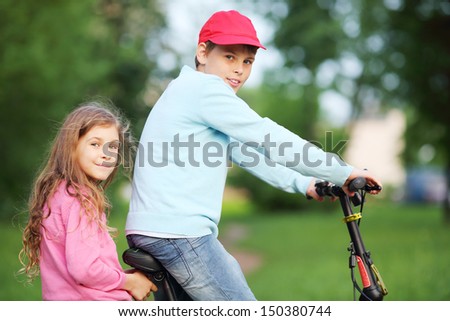 Happy brother and sister ride bicycle in park at summer day.