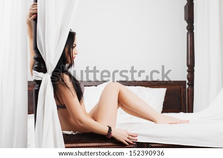 Young woman in underwear sit on the bed with a canopy leaning on column