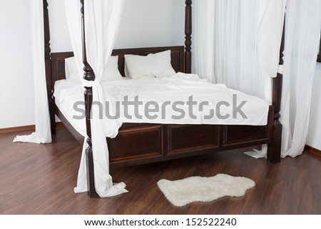 Wooden Canopy Bed And A White Hide On The Floor In A Light Room