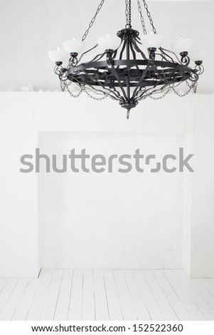 Vintage black chandelier with candles in an empty room with white walls and floors