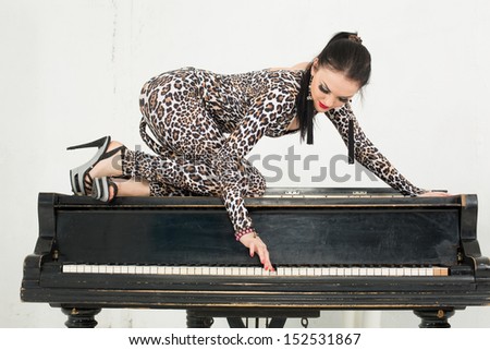 A beautiful young woman in a suit with an animal coloring sits on the piano and presses a key