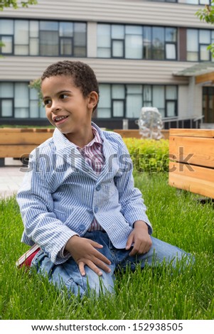 The boy in the striped jacket sitting on his knees on the grass