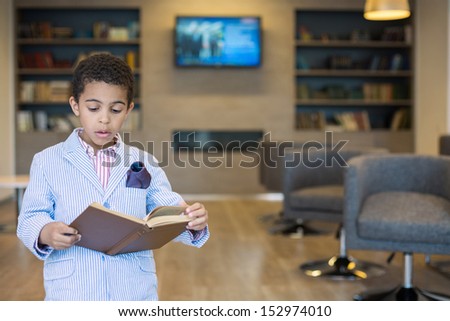 Mulatto boy in a striped jacket read a book in library