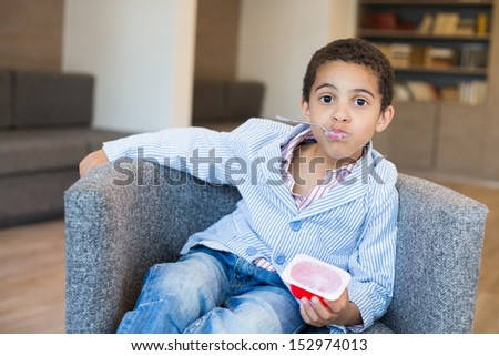 Little mulatto boy with spoon in mouth eating yogurt in the business center