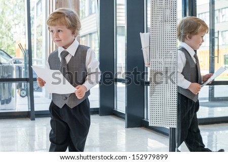 Little boy in business clothes with a magazine in the business center