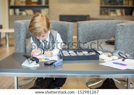Little cute boy in business clothes draws the diagram on the table.