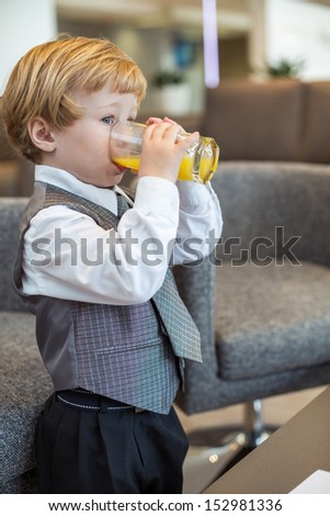 A little boy in a business clothes drinking juice in the business center