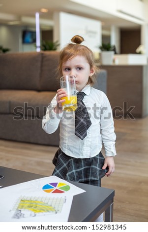 A cute little girl in a business clothes drinking juice in the business center