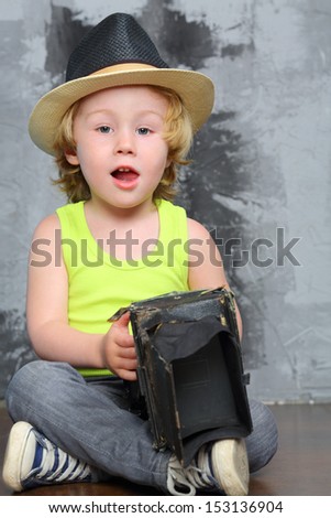 Small boy in hat sits on the floor with old camera