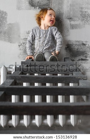 Little red-haired girl sitting on a stairs and making faces