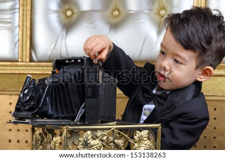 Portrait of a little boy in black tuxedo with old camera
