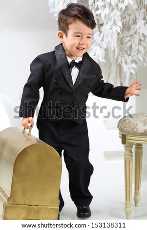 Portrait of a little boy in black tuxedo with old case