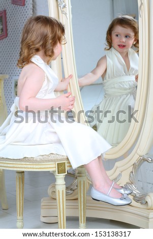 A little girl dressed admires her reflection in the large mirror