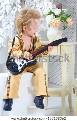 Portrait of a little boy in pop retro suit playing the guitar