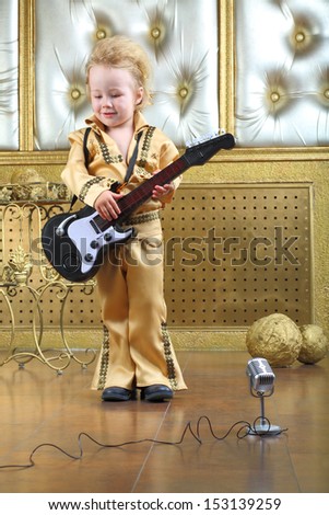 A little boy in pop retro suit playing the guitar
