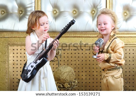 A little girl in white dress plays guitar and pop musician sings a song