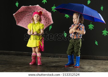 Little boy and girl with umbrellas in bright clothes and rubber boots