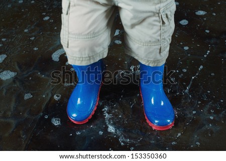 Childrens legs wearing blue rubber boots and shorts in the water