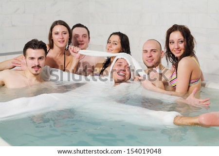 Three girls and three guys having fun in the pool pulling the ears guy in rabbit costume