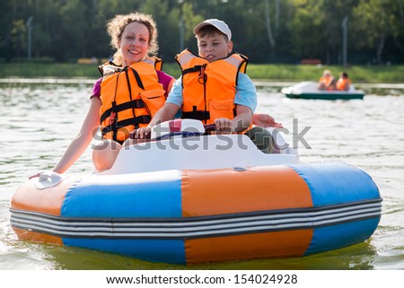 Son and mother in life jackets floating down the river in a rubber boat with electric wheel