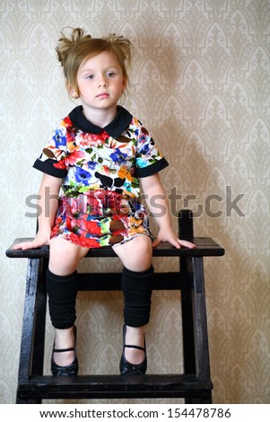 A little girl in variegated dress sitting on a black stand