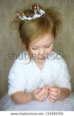 A little girl in crown looks at the rhinestones in their hands