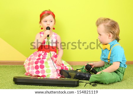Boy and girl sitting on the floor in front of a toy piano, a girl singing into a microphone