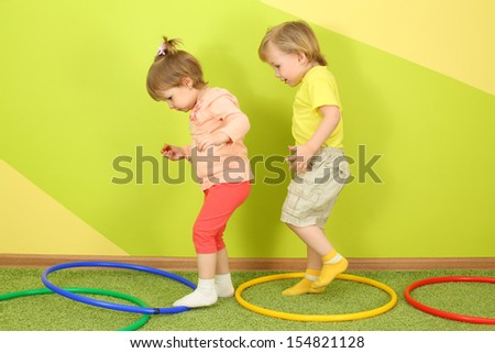 The boy runs after a girl in a bright room, on the floor are colored hoops