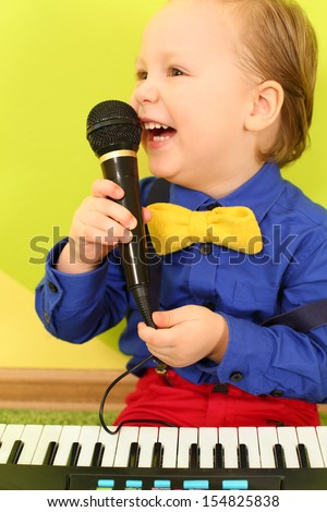 Boy in bright clothes with a toy piano singing into a microphone