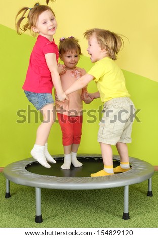 Three smiling children jumping on a trampoline holding hands