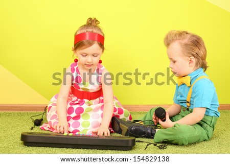 Mods boy and girl in bright clothes sitting on the floor in front of a toy piano