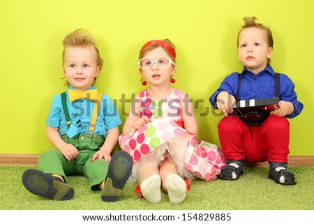 Three mods children in bright clothes sitting at the bright green wall