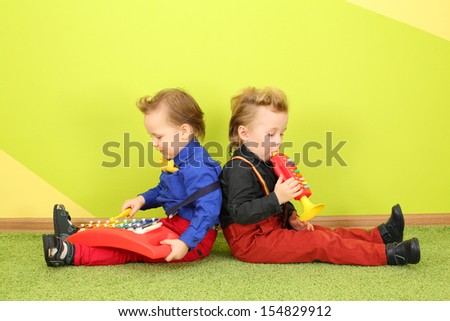 Two boys are sitting back to back and playing on a childrens trumpet and metallophone