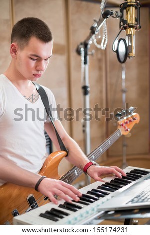 Musician with a guitar around his neck plays keyboards in the studio