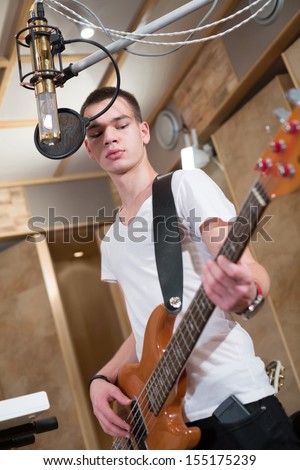 Young bass player standing with his guitar and singing into a microphone