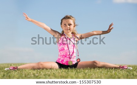 Little girl with medals sitting on the splits on the grass outdoors