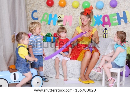 Four kids look at entertainer inflating balloon by pump at children party. Inscription Happy Birthday on wall.