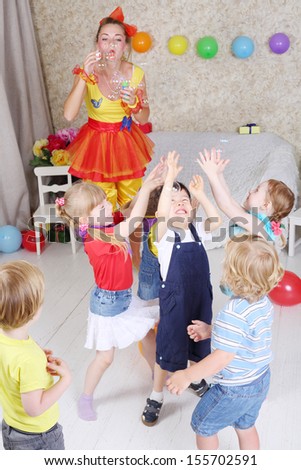 Five kids catch soap bubbles, which lets entertainer at children party.