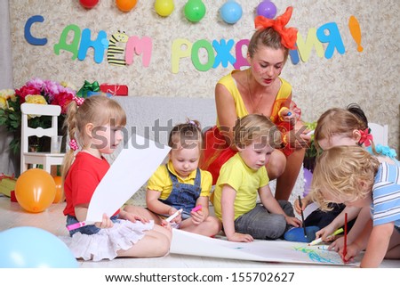 Five kids and holiday representative draw on floor at funny children party. Inscription Happy Birthday on wall.