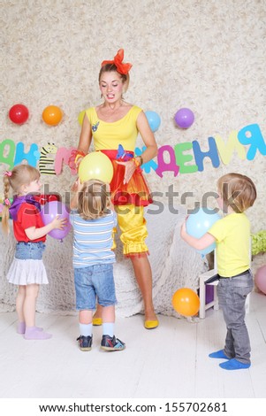 Three kids and facilitator play with balloons at funny children party. Inscription Happy Birthday on wall.