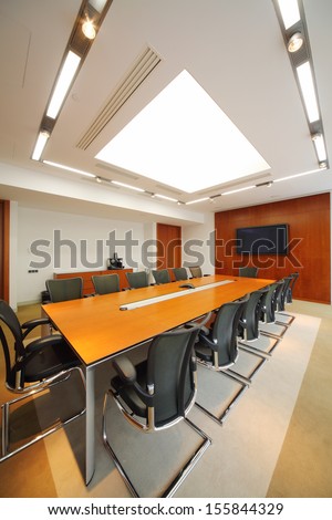 Long wooden table, black armchairs and tv in light room for business meetings.