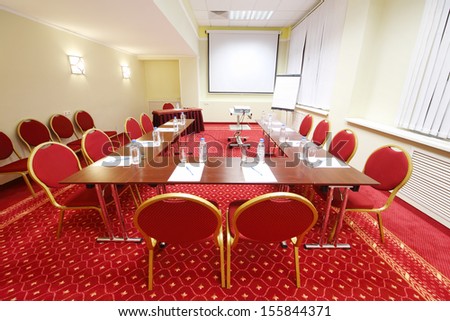 Projector, red chairs and tables with bottles in small room for business meetings.