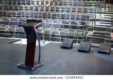 Document stand on black stage and rows of seats in empty concert hall.